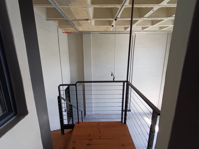 An industrial-style landing area featuring a timber staircase, metal cable balustrades, and an exposed concrete waffle ceiling with visible conduit.
