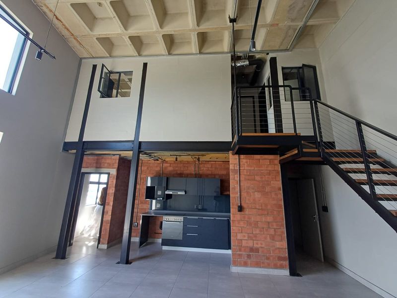 Spacious open-plan industrial-style apartment featuring exposed brickwork, a concrete waffle ceiling, a modern kitchen, and a mezzanine level with a steel staircase.