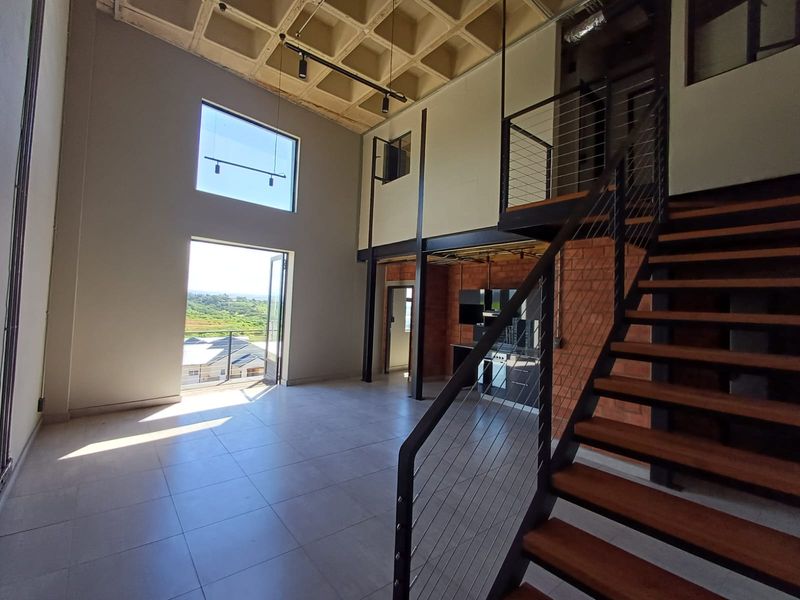 Spacious open-plan living area featuring a striking waffle slab ceiling, exposed brickwork, and a modern steel staircase leading to a mezzanine level.