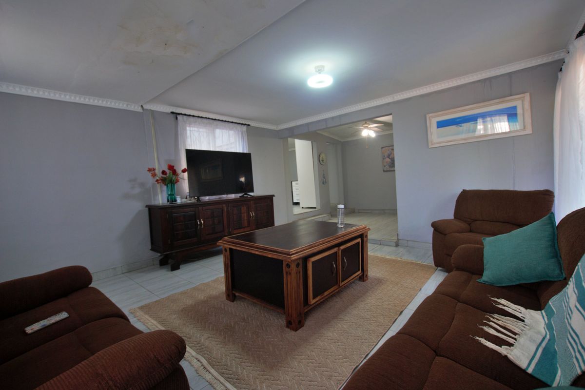 A spacious living room featuring tiled flooring, crown molding, and an open-plan layout leading to an adjacent hallway.