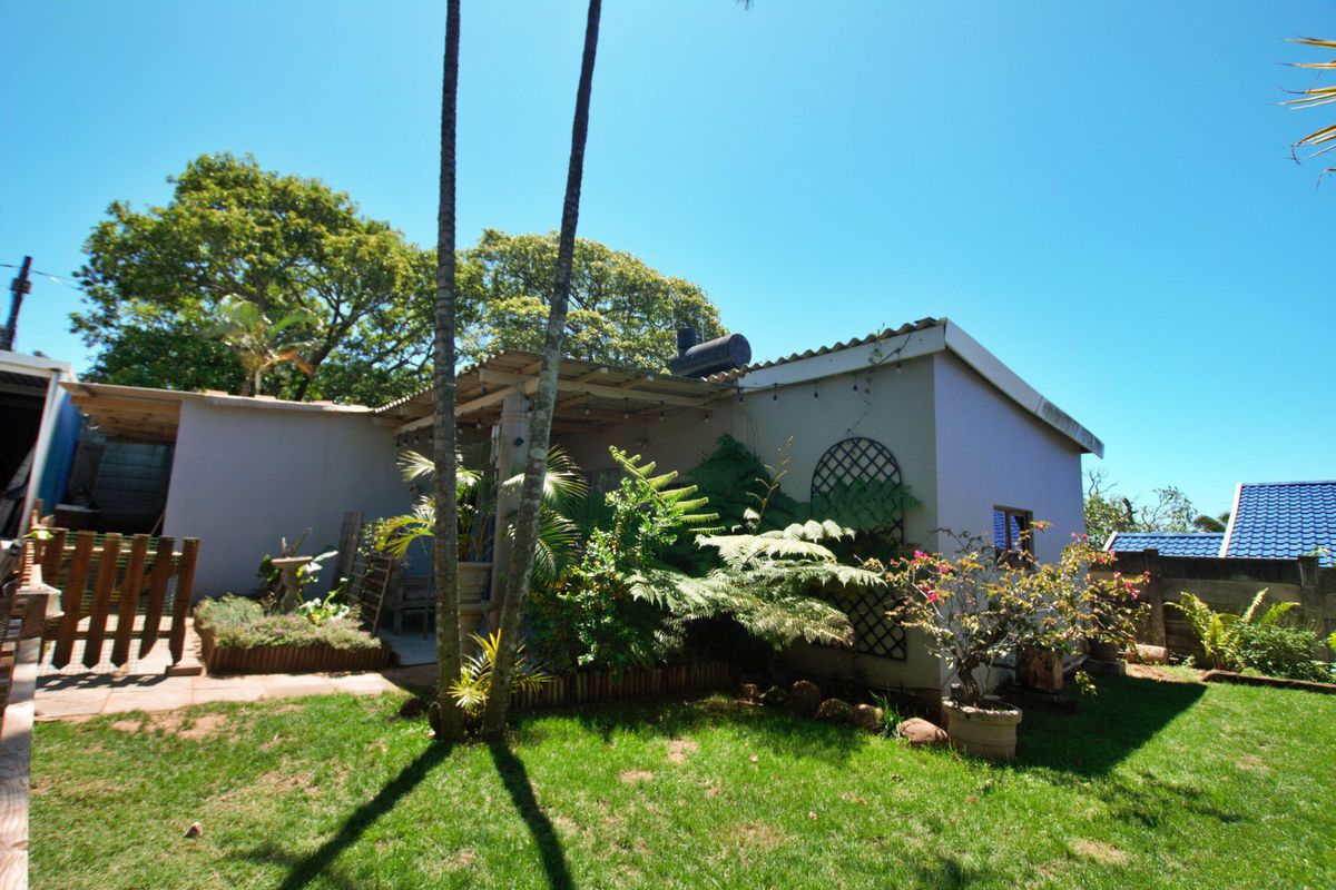 A rear view of the property featuring a covered patio area, established garden, and lawn space, providing a private outdoor living environment.
