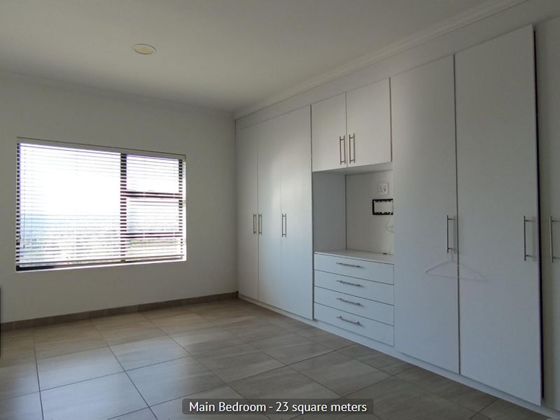 Spacious main bedroom featuring extensive built-in cupboards, neutral tiled flooring, and large windows with fitted blinds.