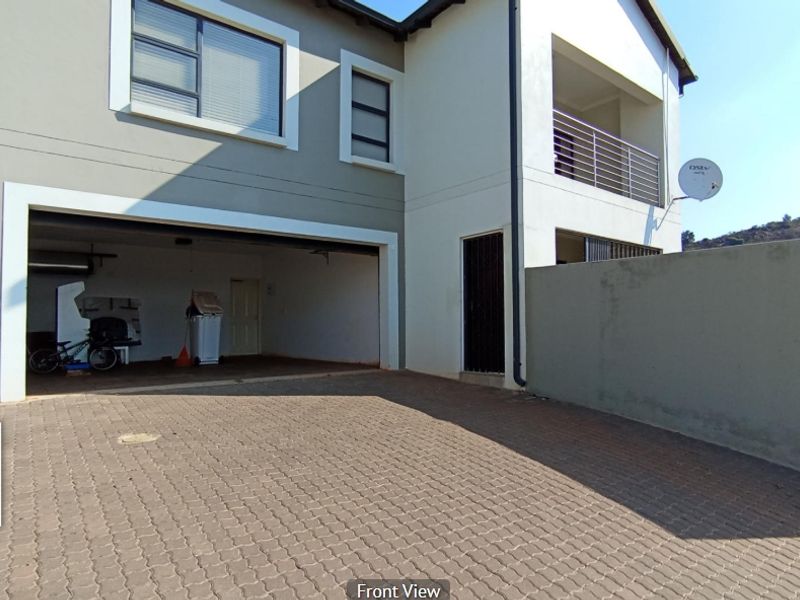Front view of a cluster home featuring a double garage, paved driveway, and an upper-level balcony.