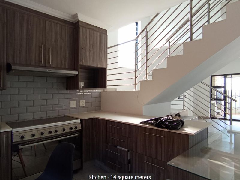 Modern kitchen featuring dark wood cabinetry, subway tile backsplash, and a stainless steel extractor fan, situated adjacent to an open staircase.