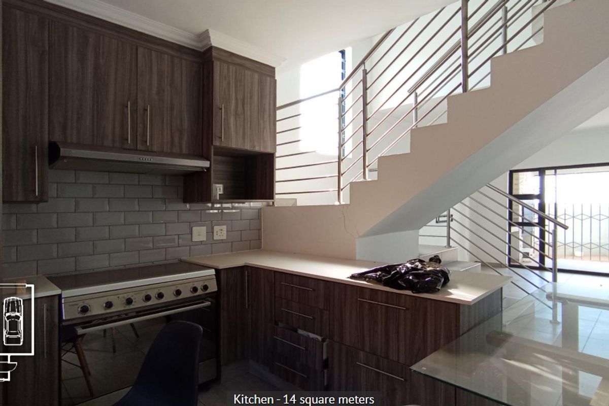 Modern kitchen featuring dark wood cabinetry, subway tile backsplash, and a stainless steel extractor fan, situated adjacent to an open staircase.