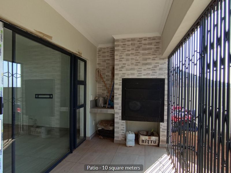 Covered patio featuring a built-in braai, stone cladding, tiled flooring, and large sliding glass doors providing access to the interior living space.