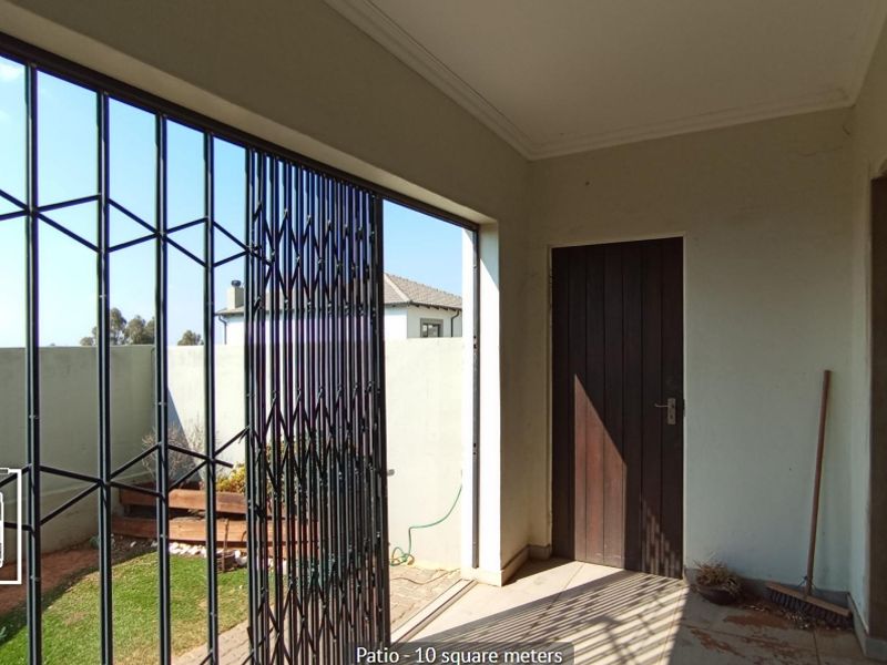 A covered patio area featuring tiled flooring, a secure metal gate, and direct access to the garden.