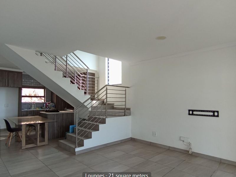Open plan living area featuring a modern staircase with stainless steel balustrades, tiled flooring, and neutral finishes, providing a versatile space for living and dining.