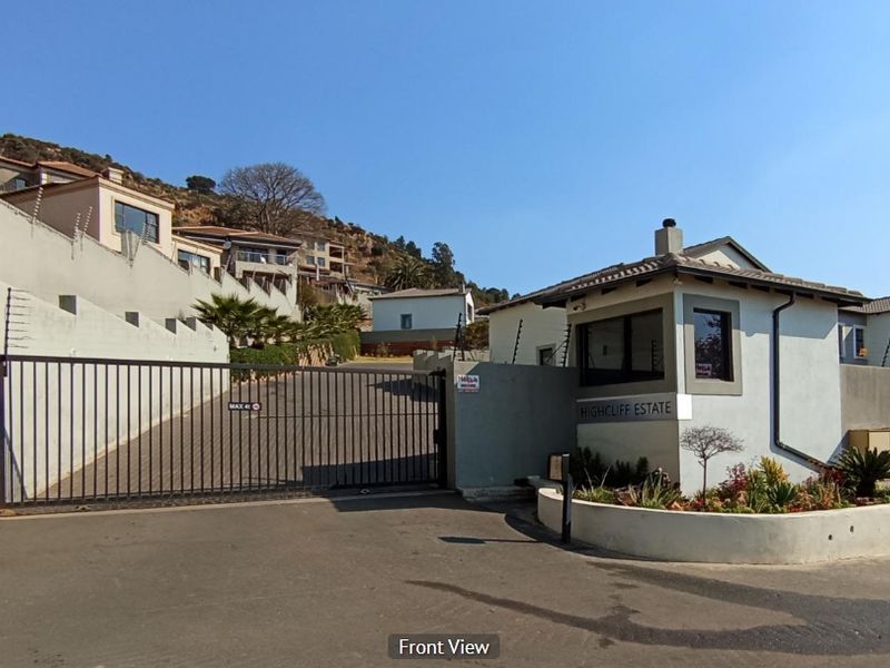 The secure entrance to Highcliff Estate featuring a gated access point, perimeter wall with electric fencing, and a dedicated security guard house.