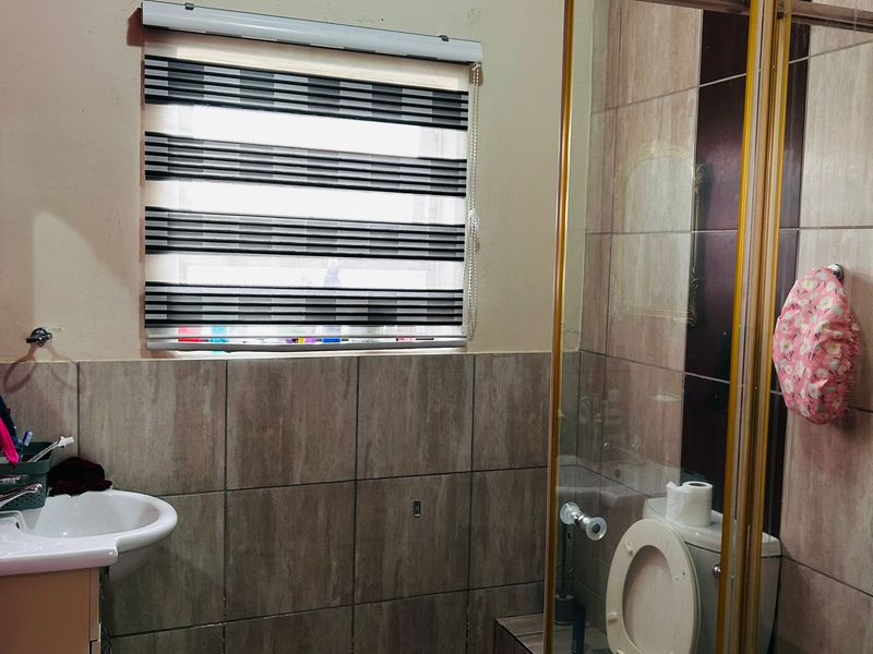 A functional bathroom featuring a pedestal basin, toilet, and a glass-enclosed shower with neutral wall and floor tiling.