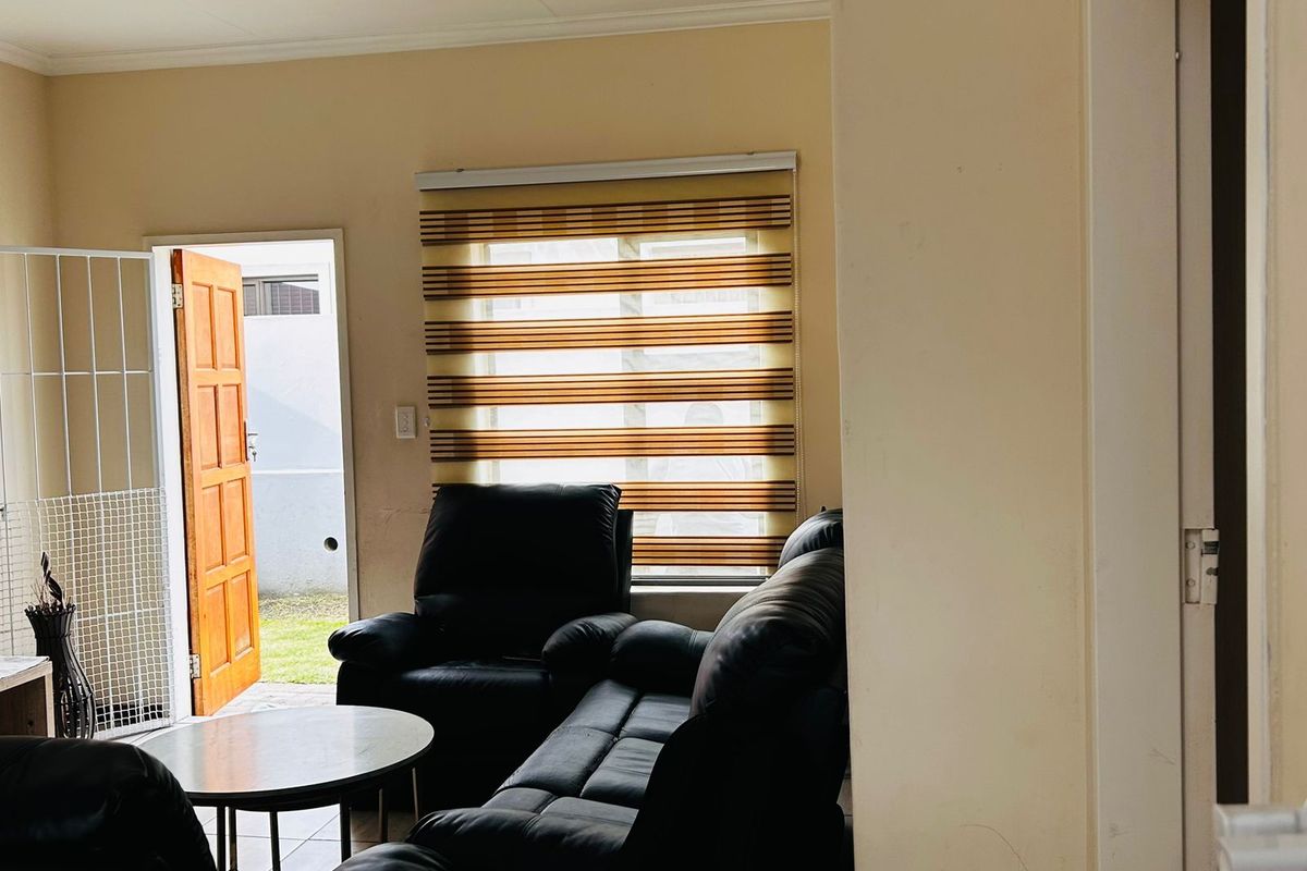 A living room area featuring zebra blinds, a security gate at the entrance, and neutral wall finishes.