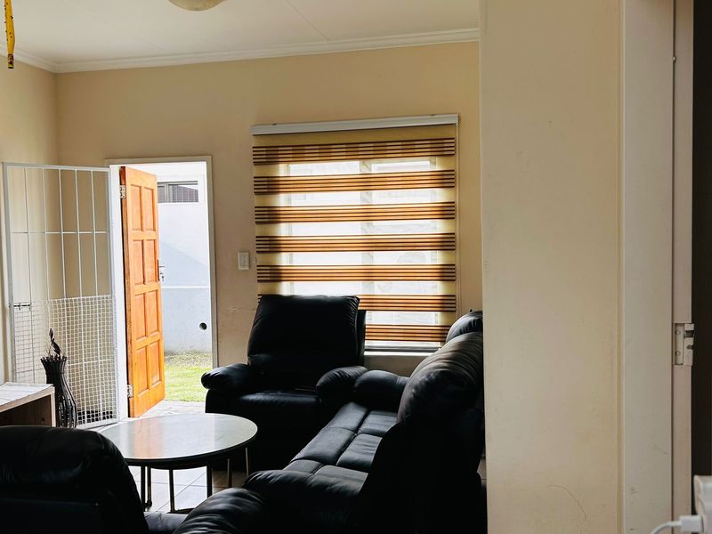 A living room area featuring a timber door leading to the exterior, zebra blinds, and a security gate.