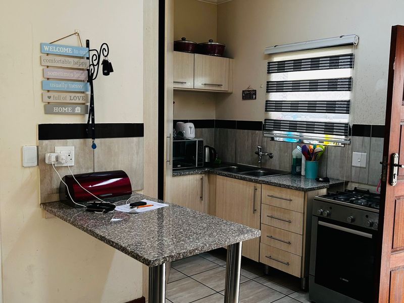 Compact kitchen featuring granite countertops, built-in cabinetry, tiled flooring, and a gas stove, offering a functional workspace with a breakfast bar extension.