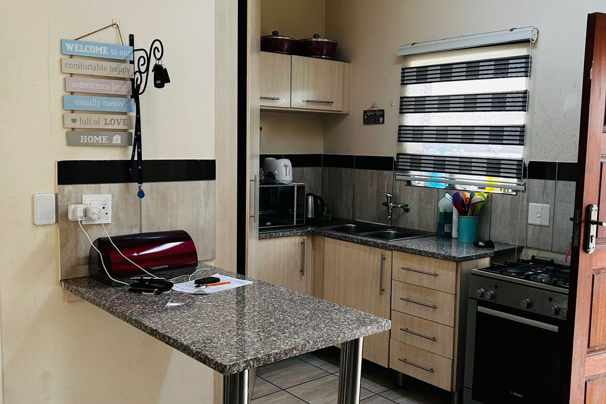 Compact kitchen featuring granite countertops, built-in cabinetry, tiled flooring, and a gas stove, offering a functional workspace with a breakfast bar extension.