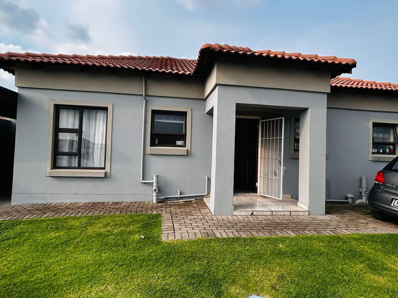 Front elevation of a townhouse featuring a terracotta tiled roof, paved entrance walkway, and a secure gated entryway with a small front lawn.