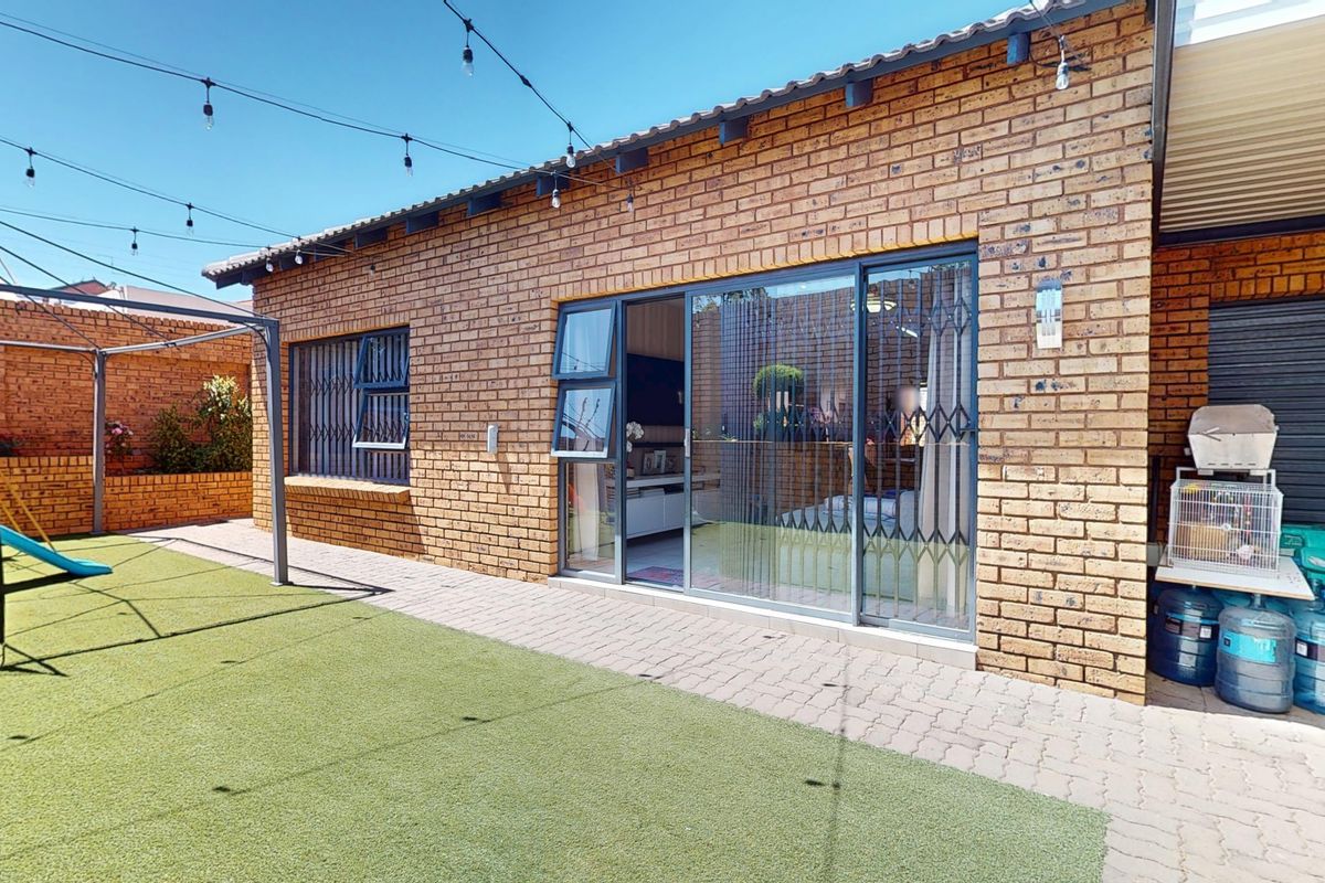 Rear exterior view of a townhouse featuring a face brick facade, paved patio area, artificial lawn, and sliding glass doors with security gates.