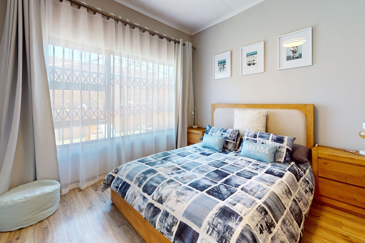 A well-maintained bedroom featuring laminate flooring and a large window fitted with a security gate and curtain tracks.