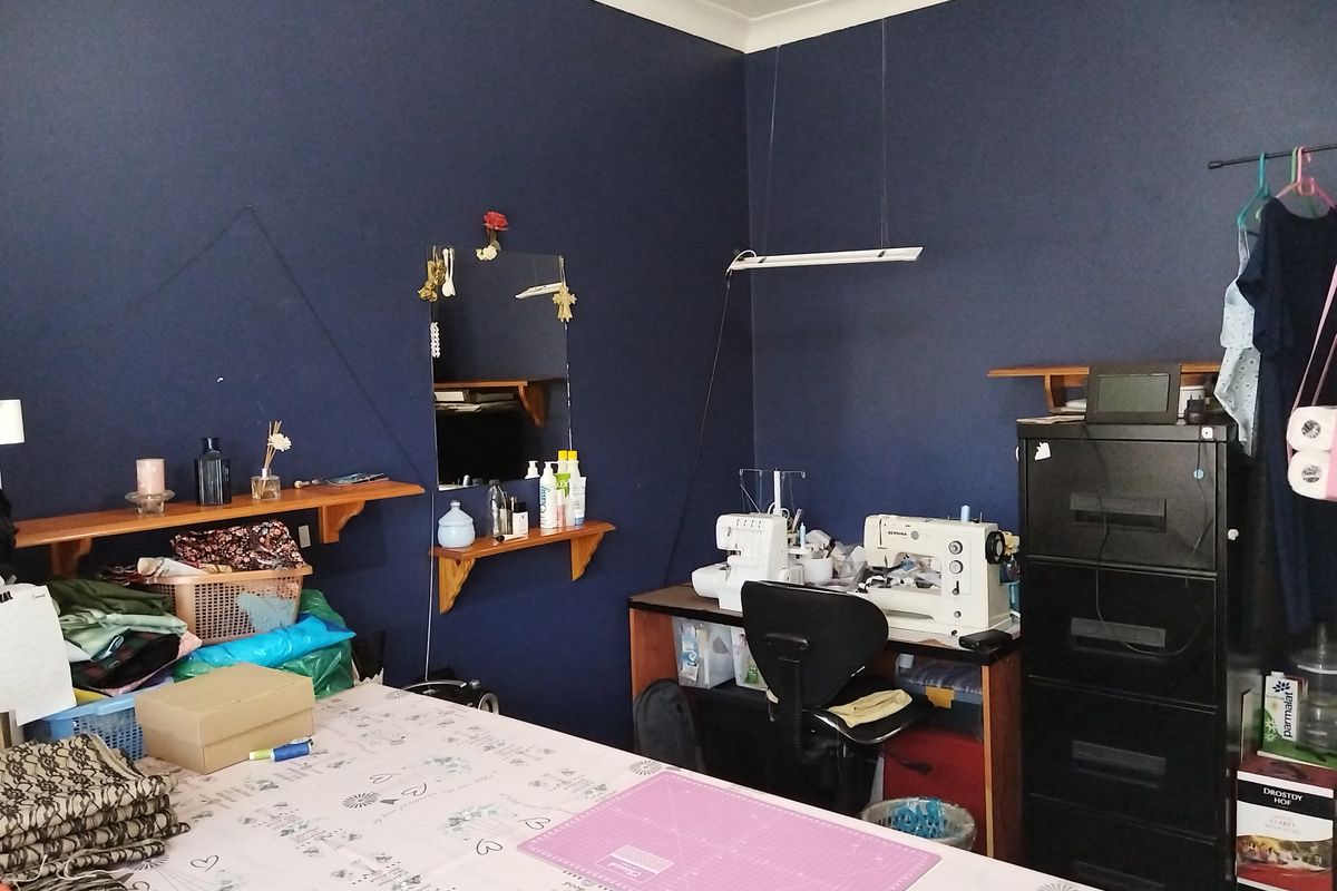 A bedroom currently utilized as a craft and sewing room, featuring dark blue walls and built-in wall shelving.