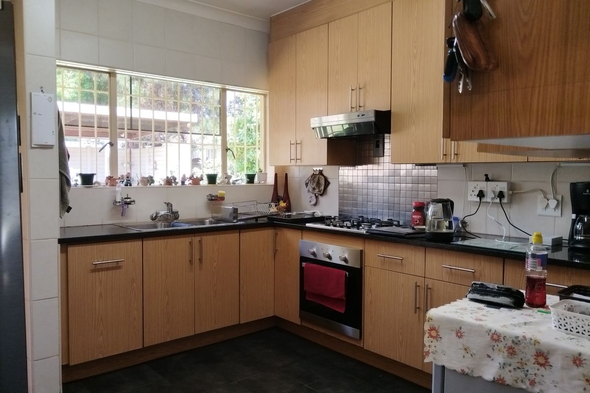 A functional kitchen featuring light wood-finish cabinetry, granite countertops, a built-in oven with gas hob, and a tiled backsplash with a large window.