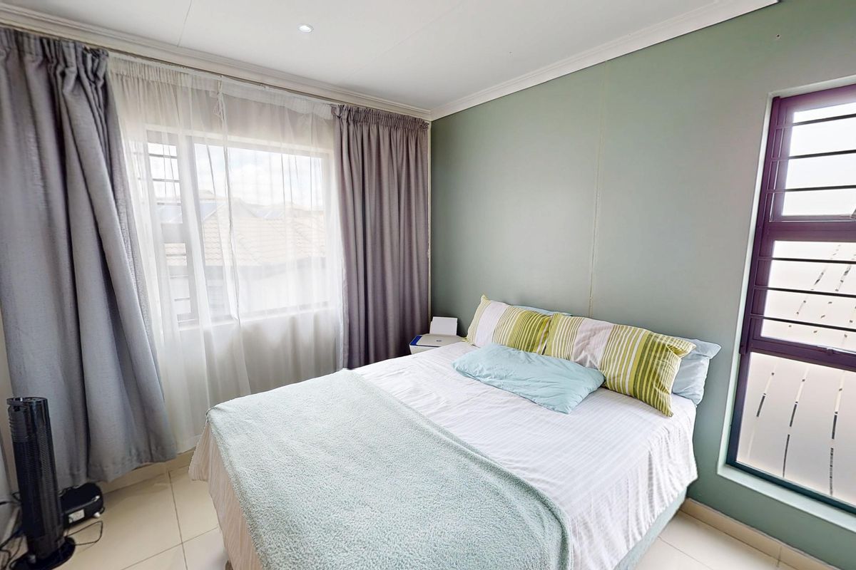 A well-lit bedroom featuring tiled flooring, neutral wall tones, and large windows with security bars, providing a comfortable and functional living space.