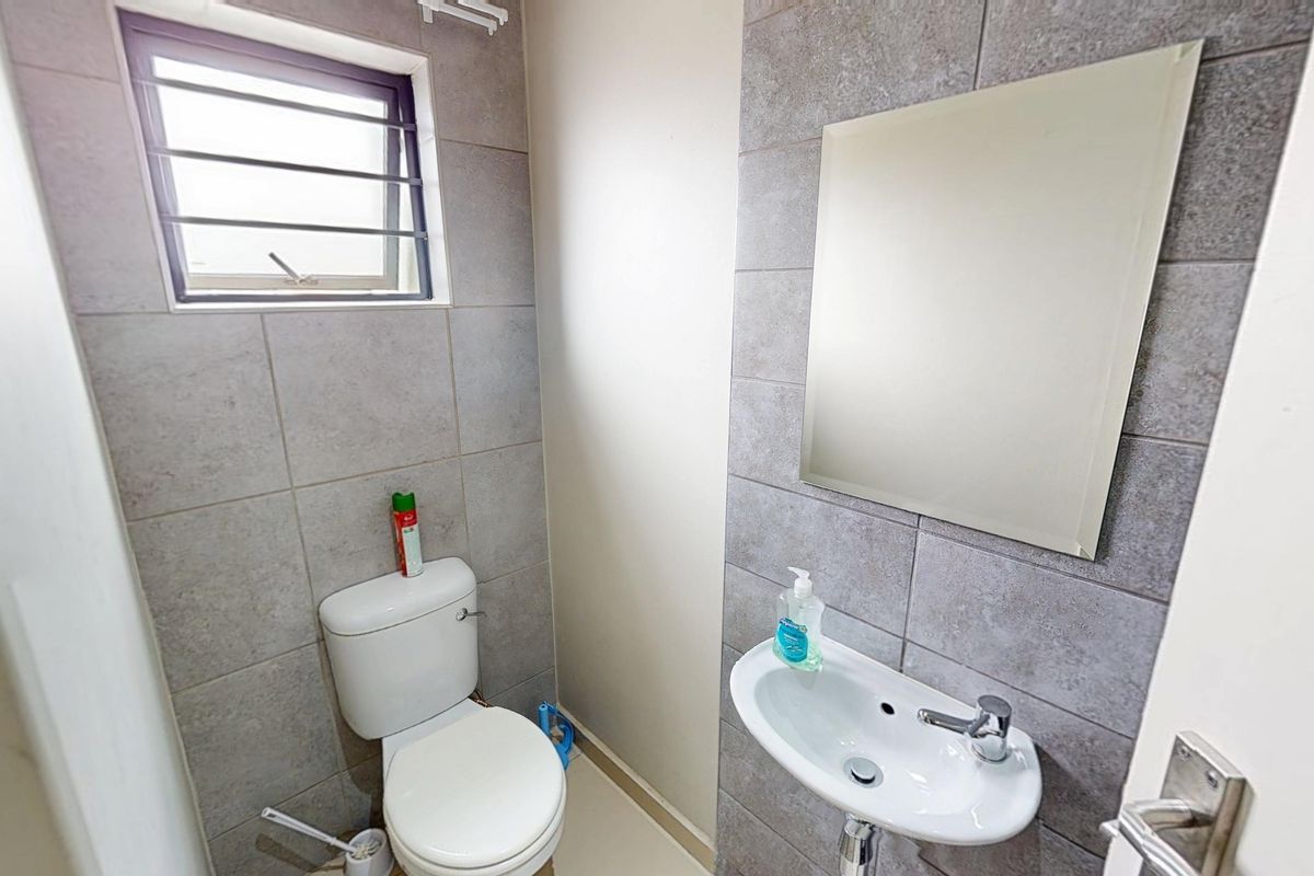 A compact, modern guest bathroom featuring neutral grey wall tiles, a wall-mounted basin with a mixer tap, and a functional toilet.