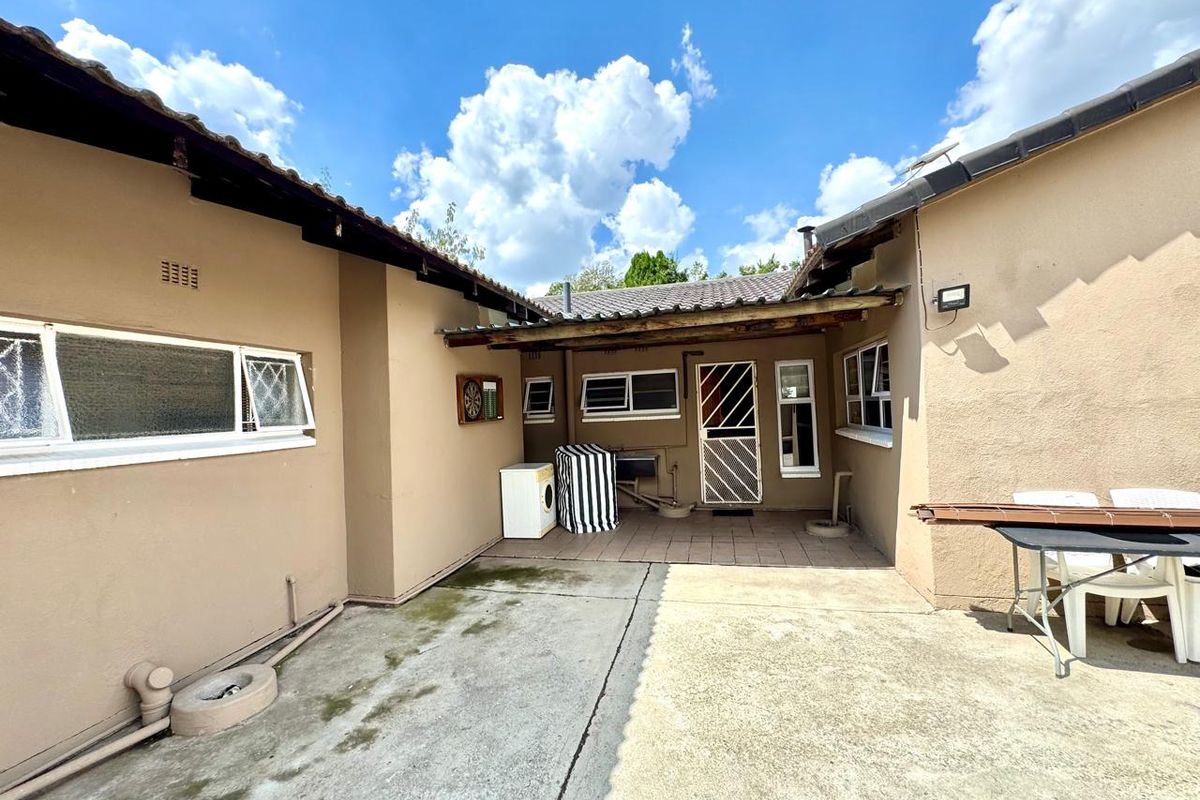 A rear exterior view of the property featuring a paved courtyard area, covered patio section, and access to the home's rear entrance.