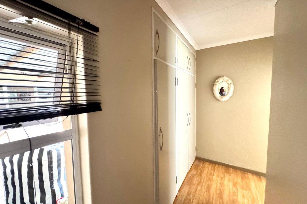 A bedroom featuring built-in cupboards, laminate flooring, and a window with fitted blinds.