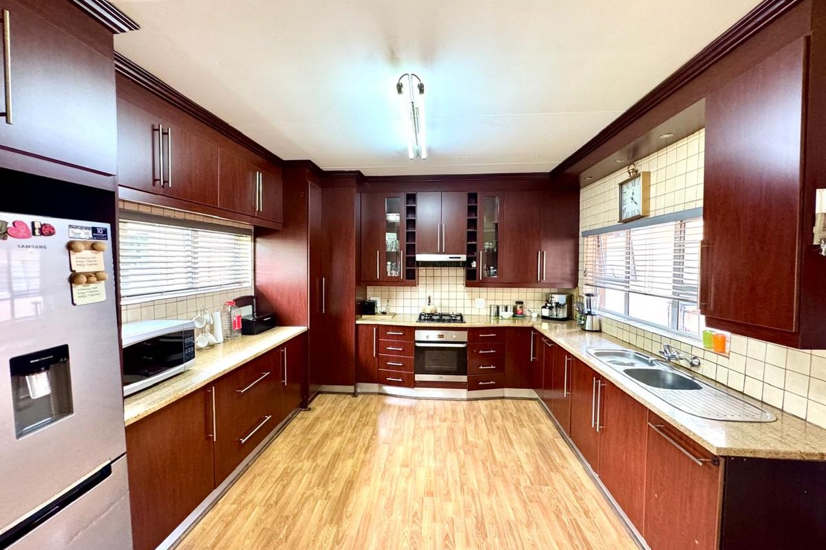 A spacious kitchen featuring dark wood cabinetry, granite countertops, a built-in oven, gas hob, and double stainless steel sink with tiled splashbacks.