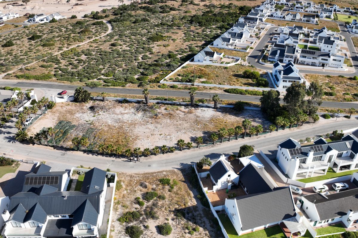 Aerial view of a coastal residential estate featuring modern homes with dark pitched roofs, paved roads, and surrounding natural landscape.