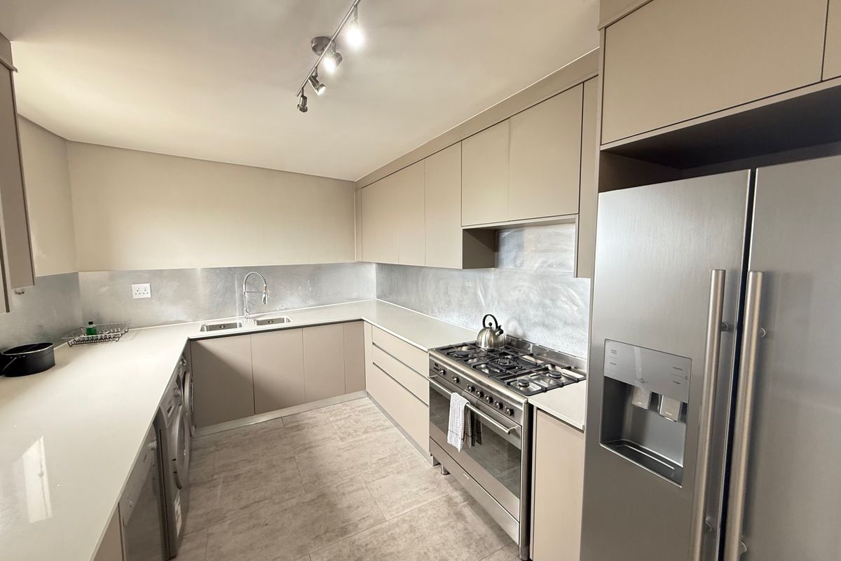 Modern kitchen featuring sleek cabinetry, stone countertops, a gas hob with oven, and integrated stainless steel appliances in a neutral color palette.