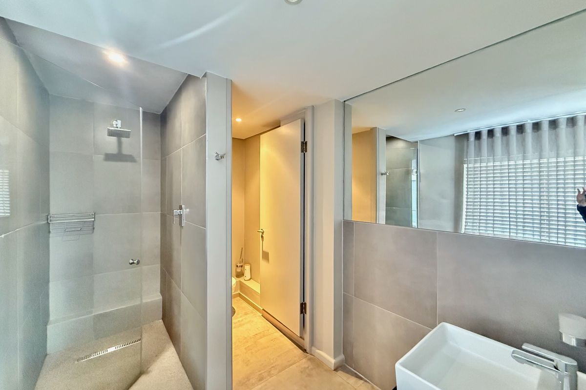 Modern bathroom featuring a walk-in shower with glass screen, wall-mounted basin, and a large vanity mirror with neutral tiling throughout.