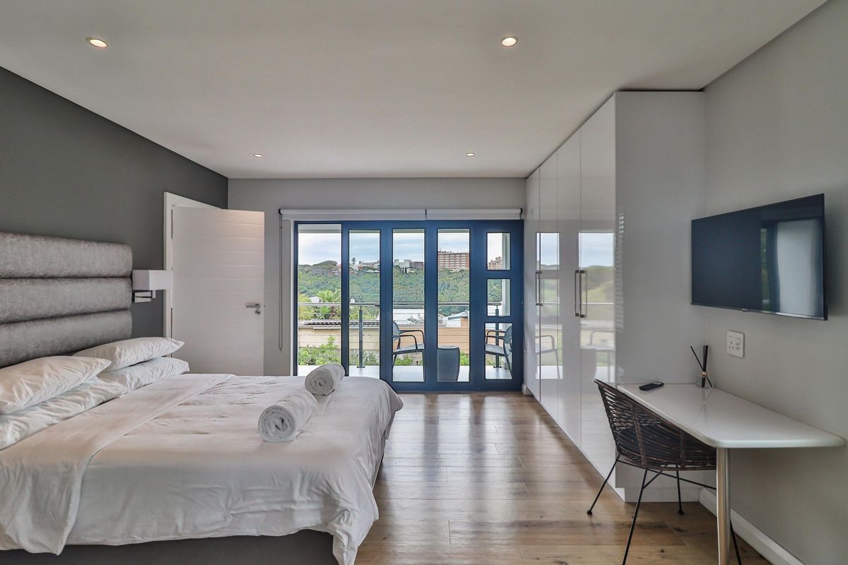 Modern bedroom featuring sleek built-in cupboards, laminate flooring, recessed lighting, and large sliding doors opening onto a private balcony with scenic views.