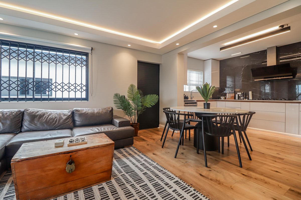 Modern open-plan living and kitchen area featuring hardwood flooring, recessed cove lighting, and a sleek kitchen with stone backsplash and integrated cabinetry.
