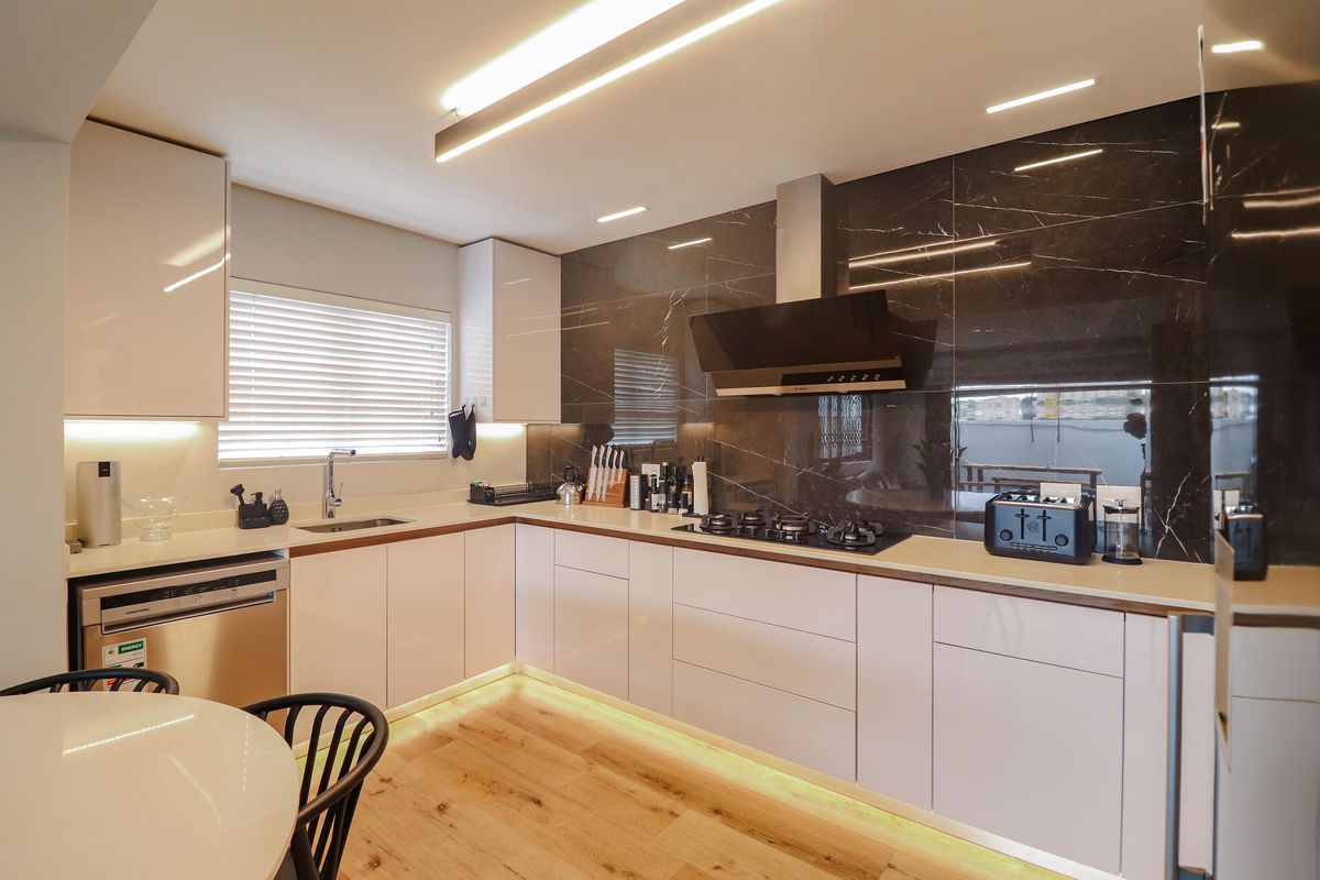 Modern kitchen featuring sleek white cabinetry, stone countertops, a dark marble-look splashback, integrated appliances, and ambient under-cabinet lighting.