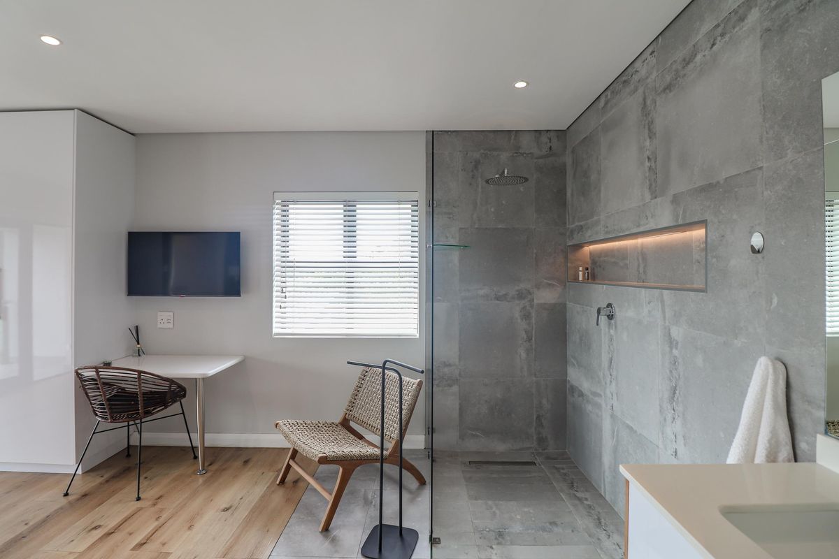 Modern open-plan bathroom featuring a spacious walk-in shower with large-format grey tiling, recessed niche lighting, and a sleek built-in vanity area.