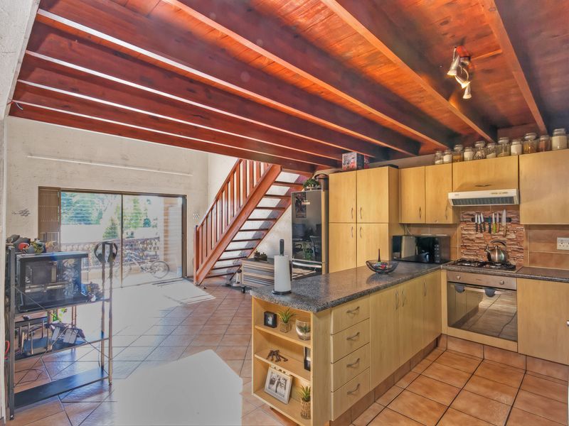 Open-plan kitchen and living area featuring exposed timber beams, tiled flooring, a timber staircase, and a functional kitchen with granite countertops and built-in appliances.