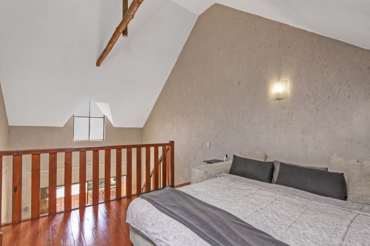 Loft-style bedroom featuring vaulted ceilings, exposed timber beams, warm timber flooring, and a wooden balustrade overlooking the lower level.