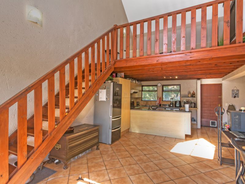 Open-plan living area featuring a wooden staircase leading to a mezzanine level, tiled flooring, and a functional kitchen with built-in cabinetry.