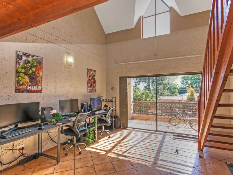 Spacious living area featuring vaulted ceilings with exposed timber beams, tiled flooring, and a timber staircase leading to an upper level.