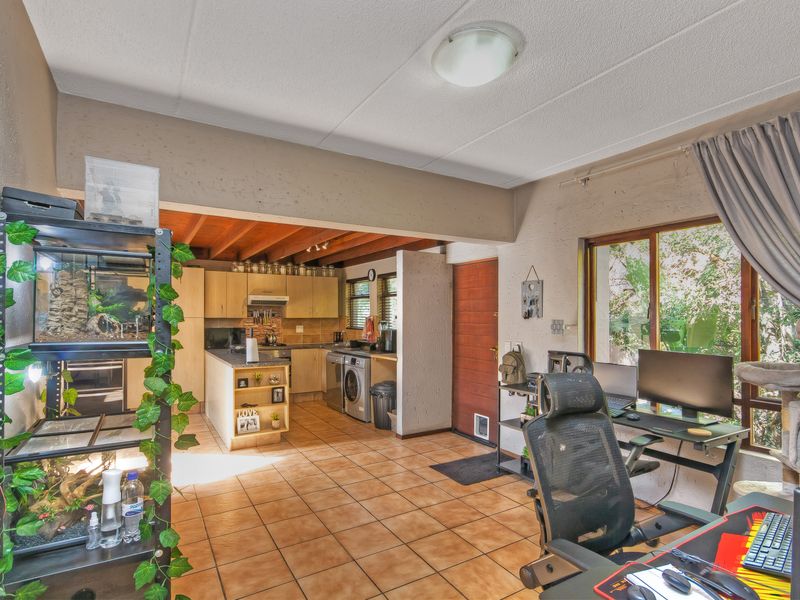 Open-plan living and kitchen area featuring tiled floors, exposed timber ceiling beams, and a functional kitchen layout with built-in cabinetry and appliances.