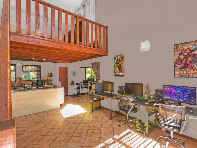 Open plan living area featuring a wooden mezzanine loft level, tiled flooring, and a functional kitchen space with an island.