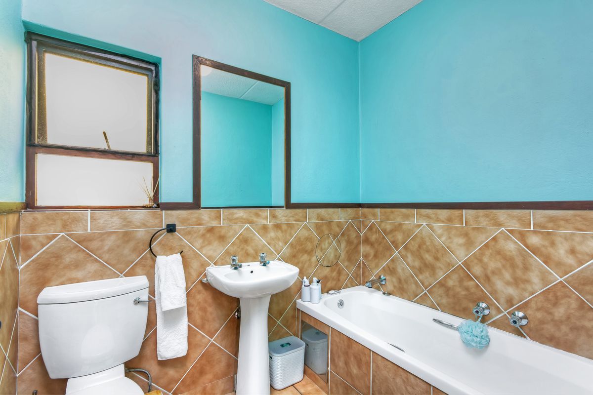 A dated bathroom featuring a pedestal basin, bathtub, and toilet with brown tiled walls and bright blue upper wall paint.