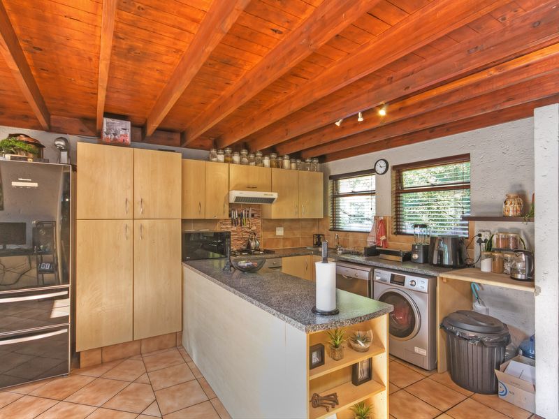 Functional kitchen featuring exposed timber beam ceilings, granite countertops, tiled backsplash, and integrated cabinetry with dedicated space for laundry appliances.