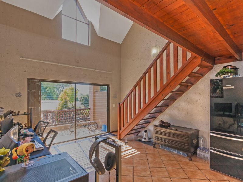 Spacious living area featuring a vaulted ceiling with exposed timber beams, a wooden staircase, tiled flooring, and large sliding doors leading to a balcony.