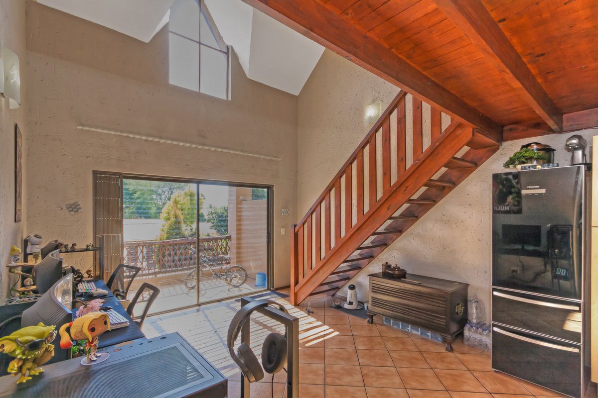 Spacious living area featuring a vaulted ceiling with exposed timber beams, a wooden staircase, tiled flooring, and large sliding doors leading to a balcony.