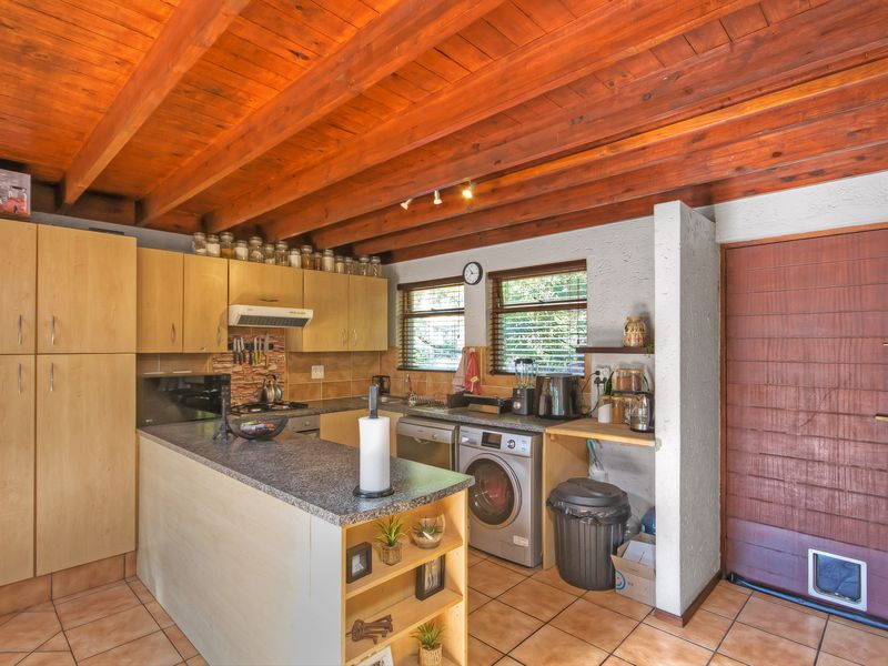 A functional kitchen featuring exposed timber ceiling beams, laminate cabinetry, granite countertops, and tiled flooring, with an integrated laundry area and direct exterior access.