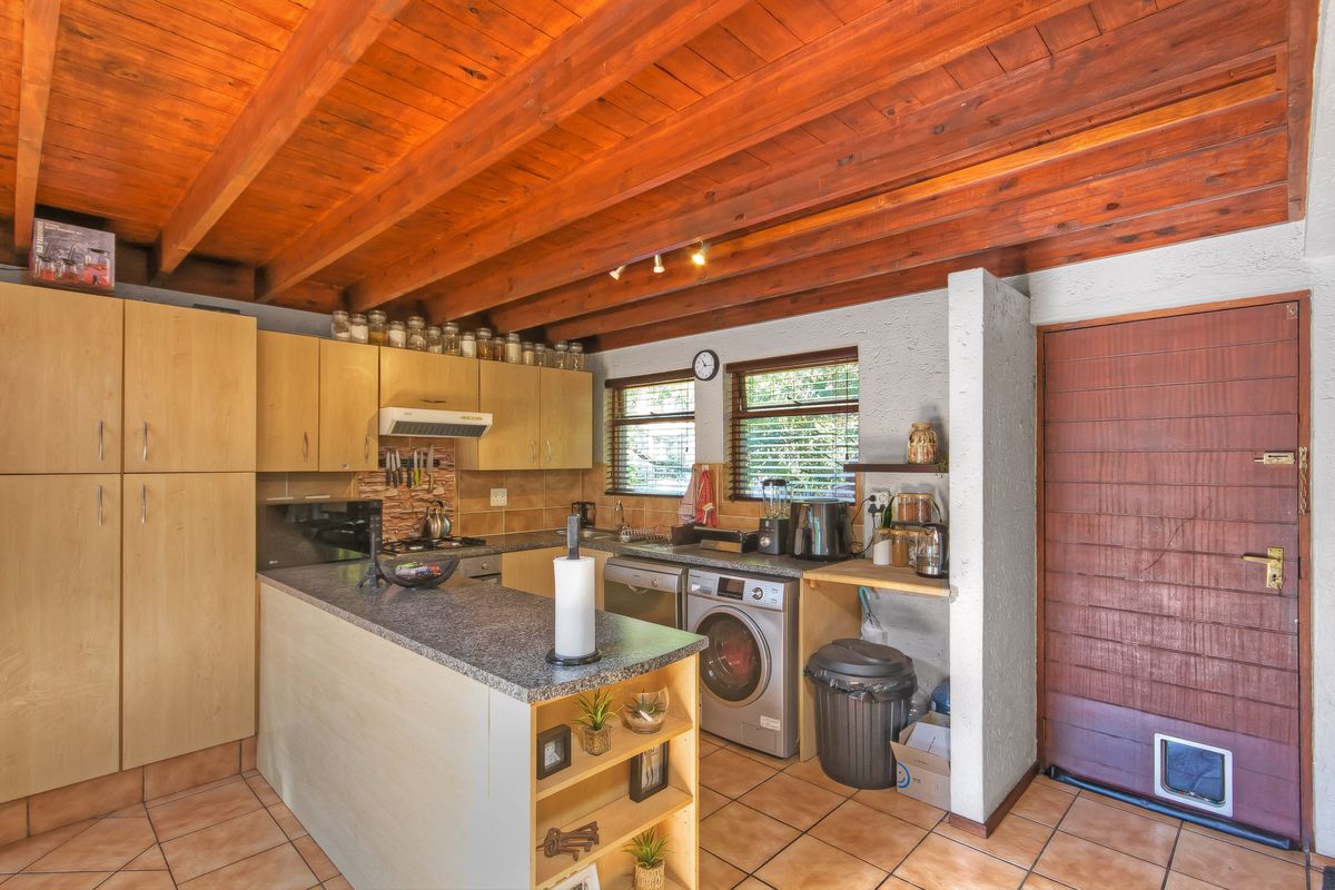 A functional kitchen featuring exposed timber ceiling beams, laminate cabinetry, granite countertops, and tiled flooring, with an integrated laundry area and direct exterior access.