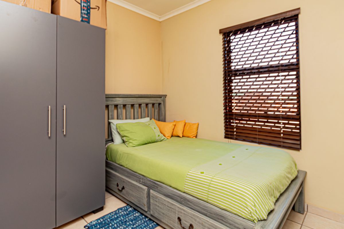 A functional bedroom featuring tiled flooring, neutral wall finishes, and fitted venetian blinds, providing a practical living space.