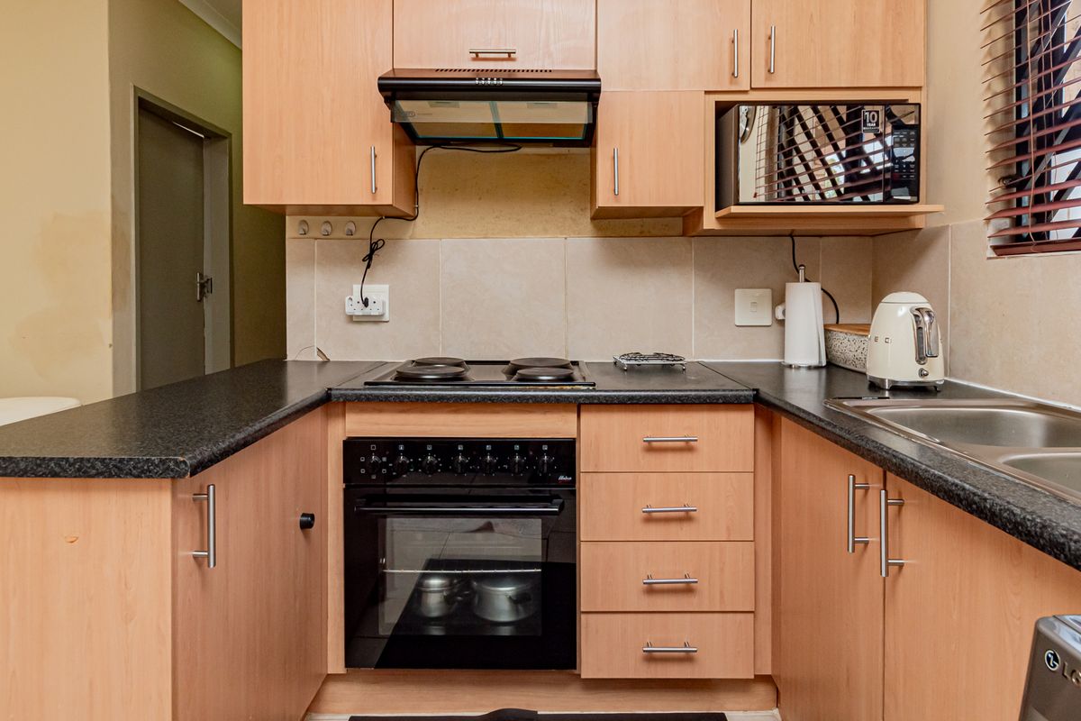 Compact kitchen featuring light wood-finish cabinetry, dark laminate countertops, built-in oven with electric hob, and a stainless steel sink.