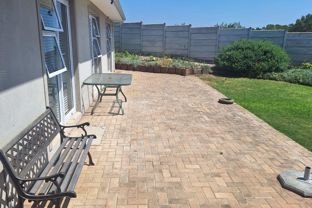A paved rear patio area featuring a brick-laid surface, adjacent to a lawn and enclosed by a concrete boundary wall.